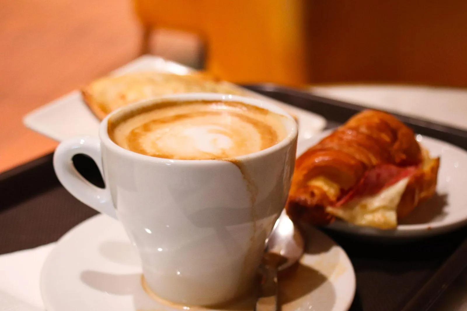 A café con leche and a croissant on a café tray