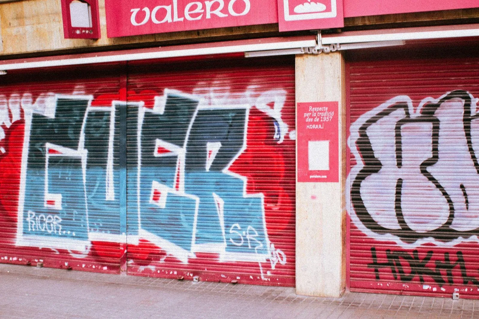 Graffiti covering red shop shutters under a Valero sign